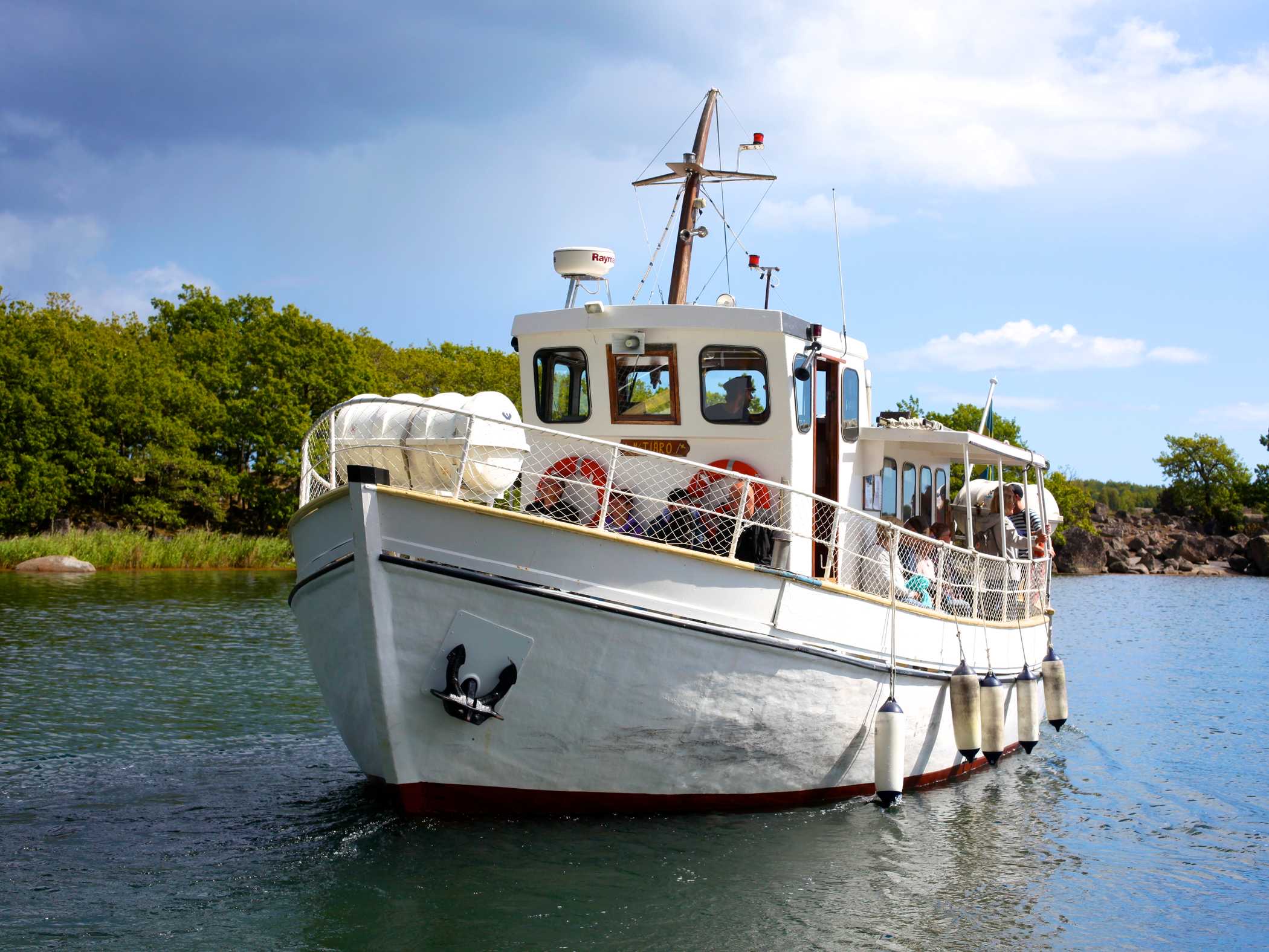 En vit skärgårdsbåt glider fram på vattnet nära en grön ö.
