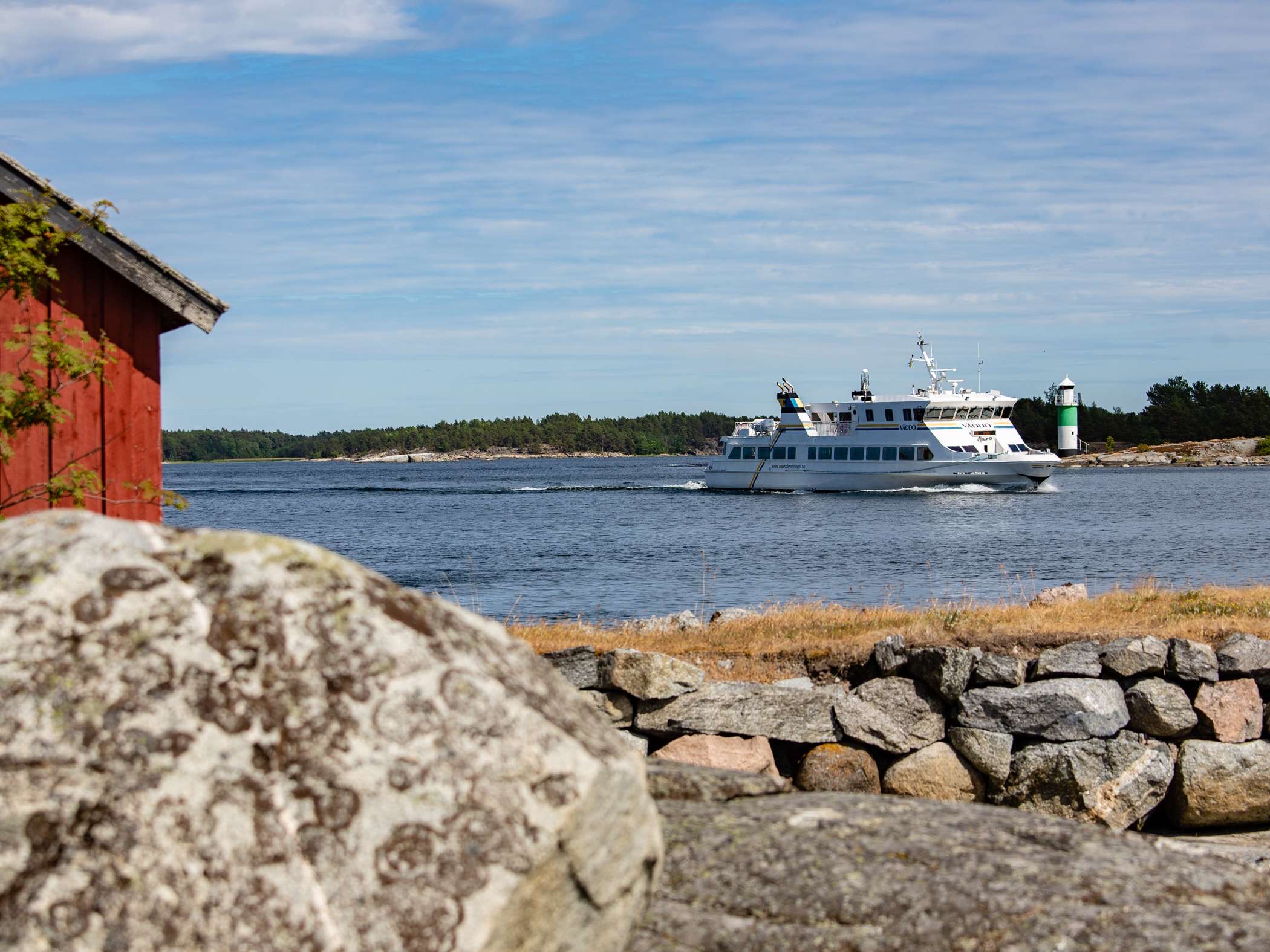 En vit passagerarbåt färdas genom skärgården med en fyr i bakgrunden. 