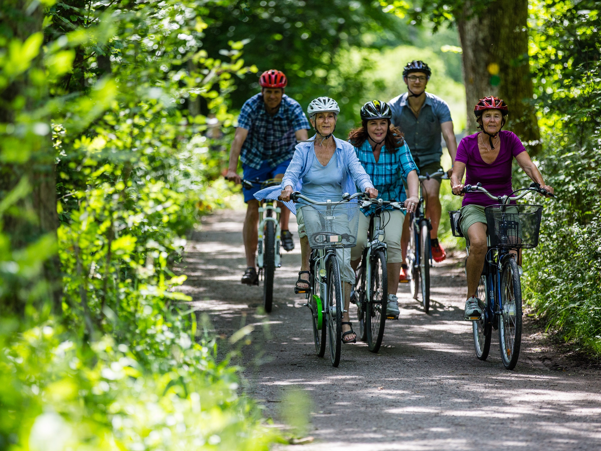En grupp människor cyklar tillsammans på en skogsväg en solig sommardag.