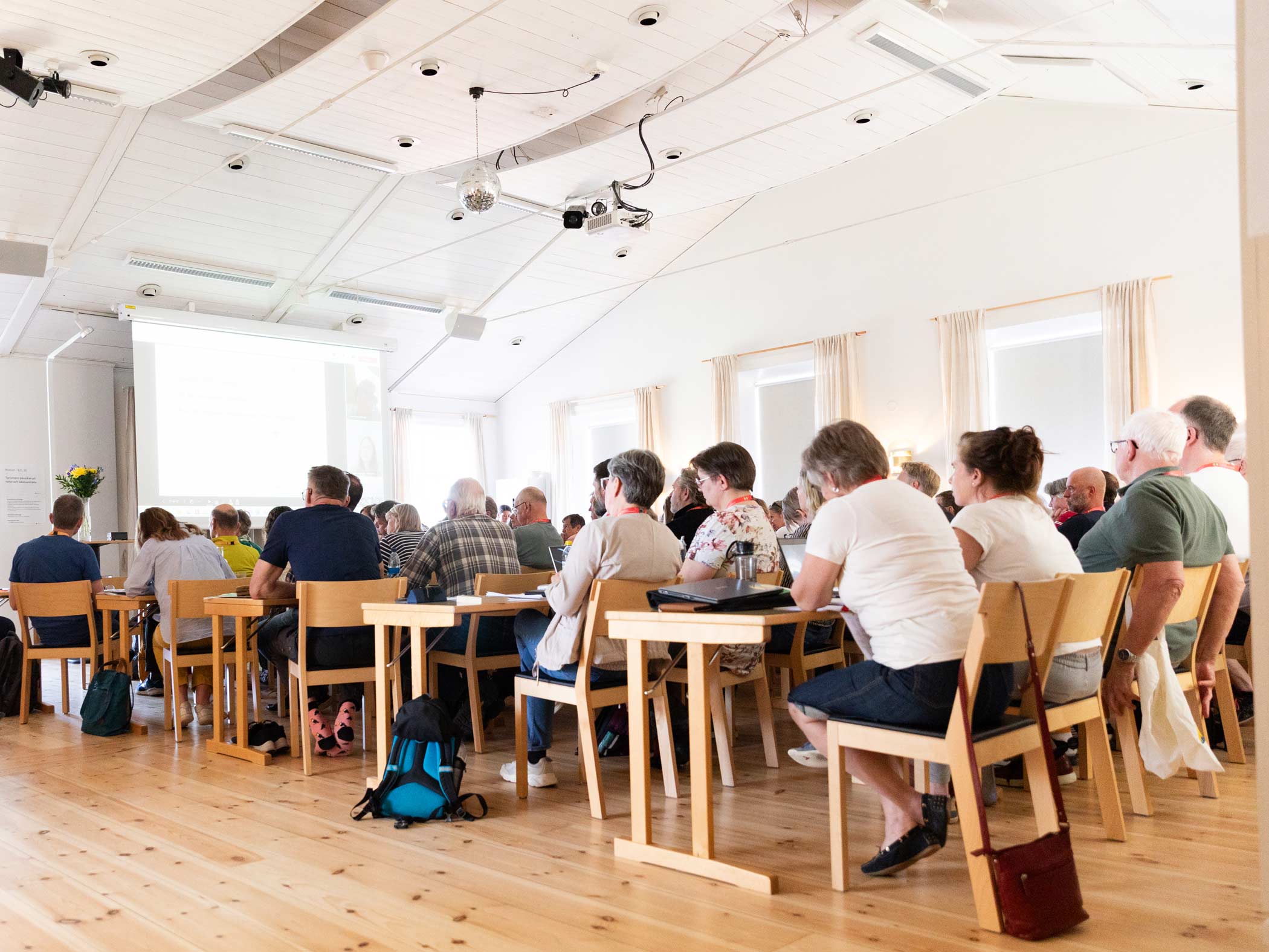 Personer lyssnar på en föreläsning i konferenslokal med projektorduk.