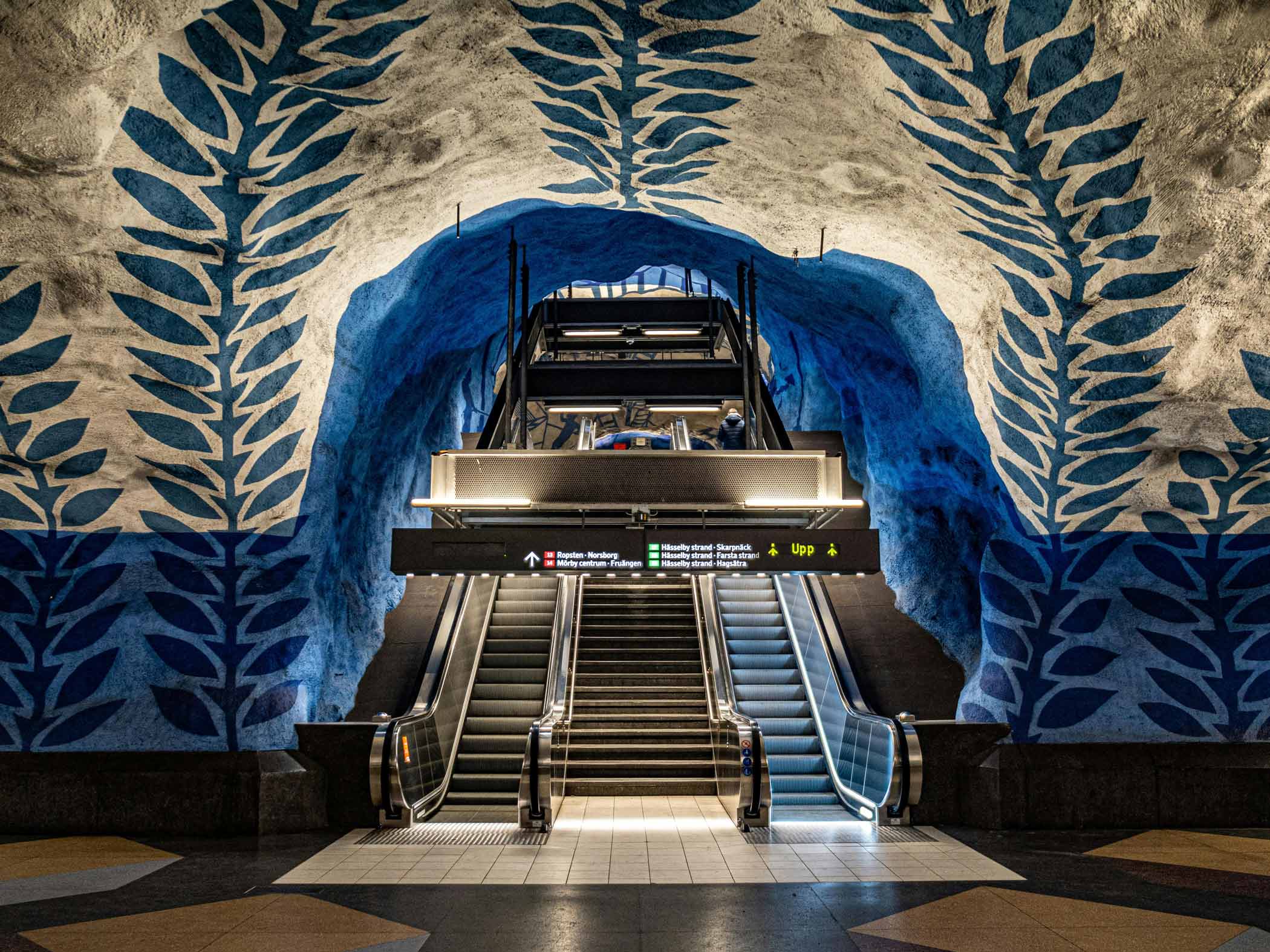 Tunnelbanestation med blå konstutsmyckning och rulltrappor.
