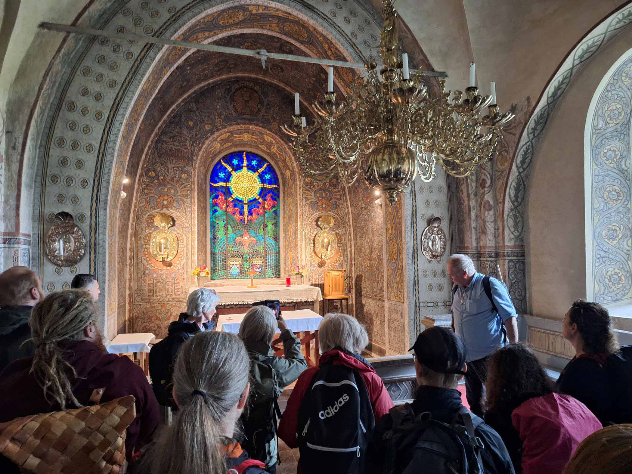 En grupp människor deltar i en guidning inne i en kyrka med färgat glasfönster.