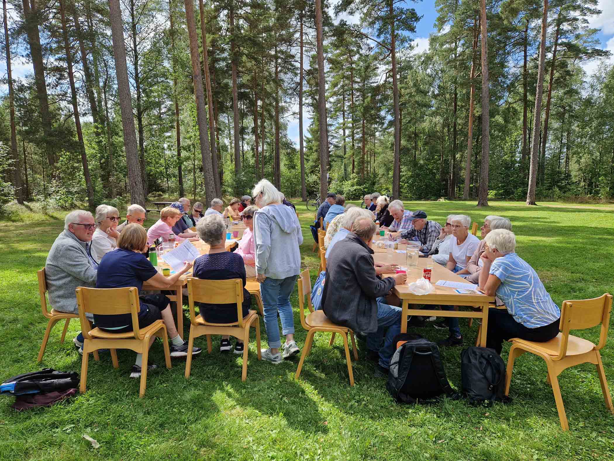 En grupp människor sitter samlade runt bord utomhus vid ett medlemsmöte.