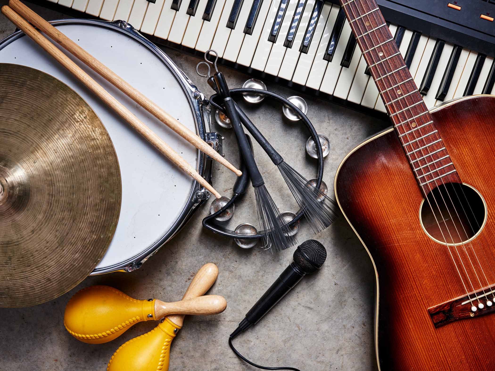 Gitarr, keyboard, trumma, tamburin och mikrofon ligger på ett golv i ett stilleben.