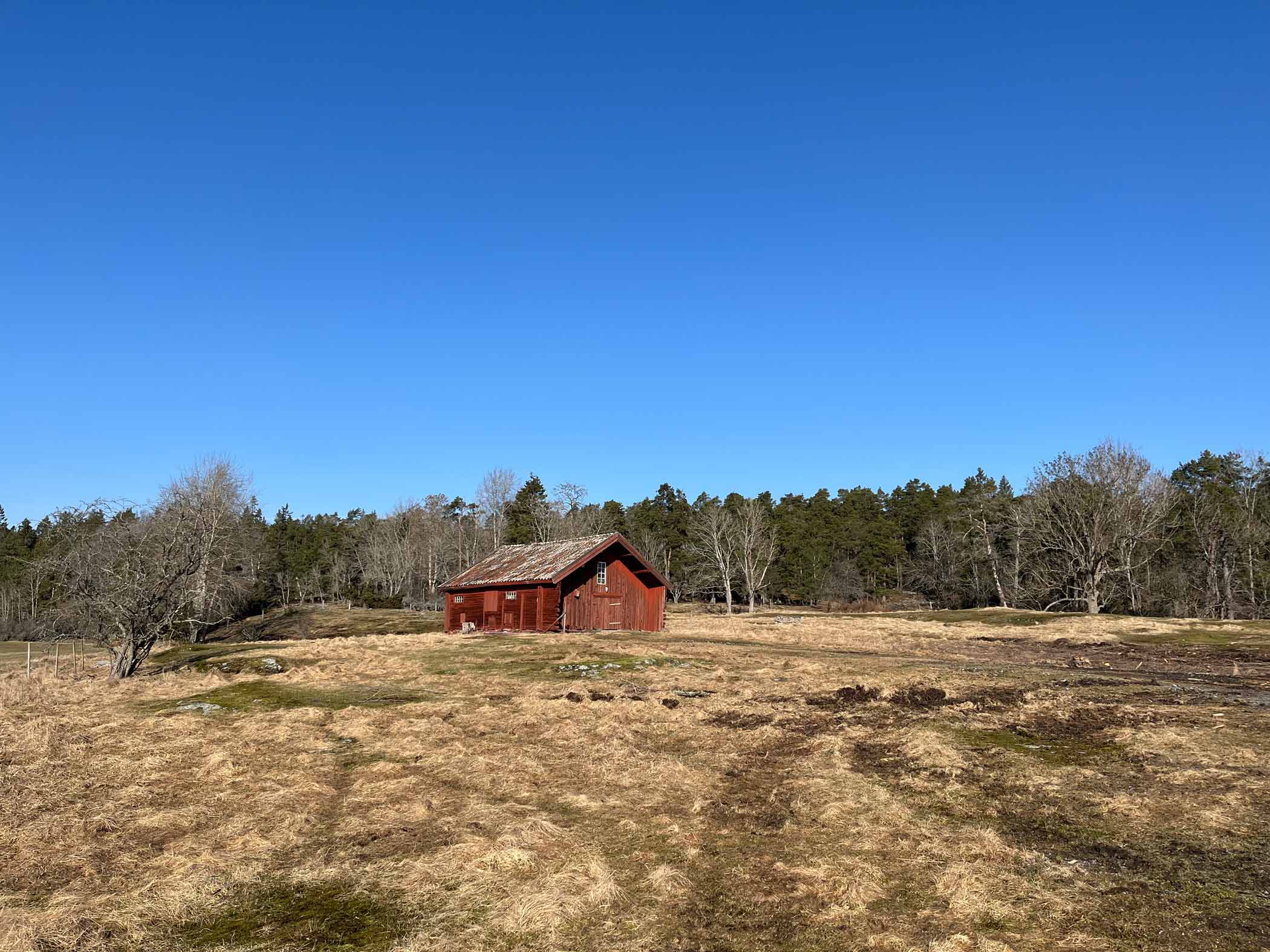 Röd stuga i öppet landskap under klarblå himmel.