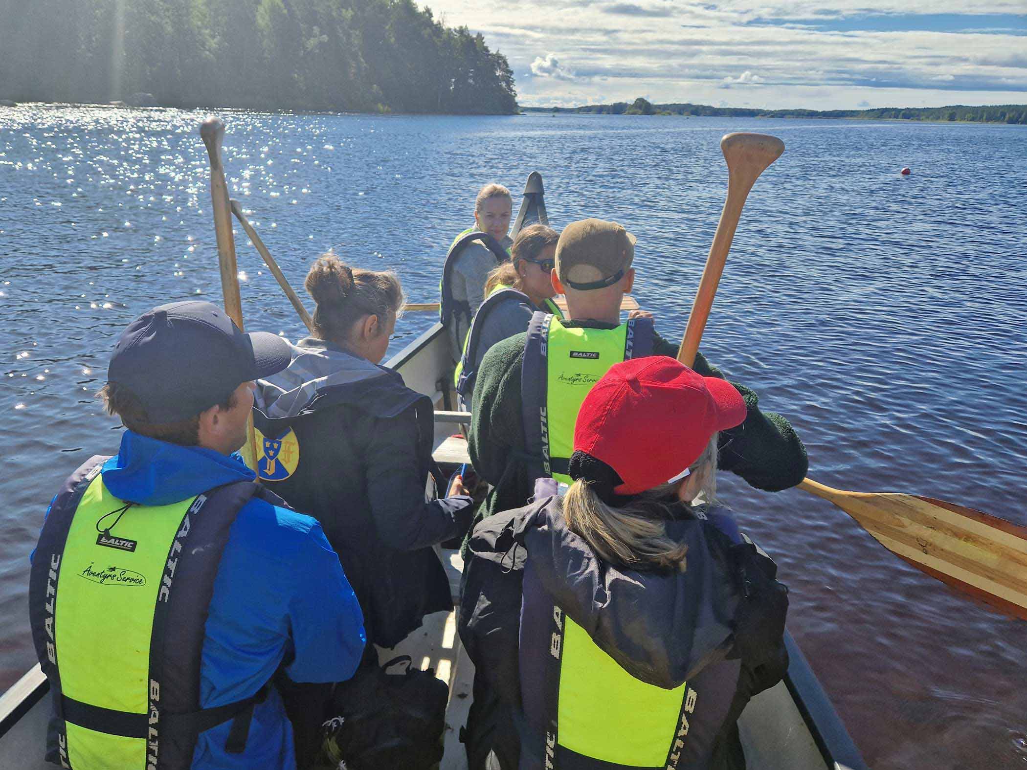 En grupp människor paddlar tillsammans i en stor kanot på öppet vatten.