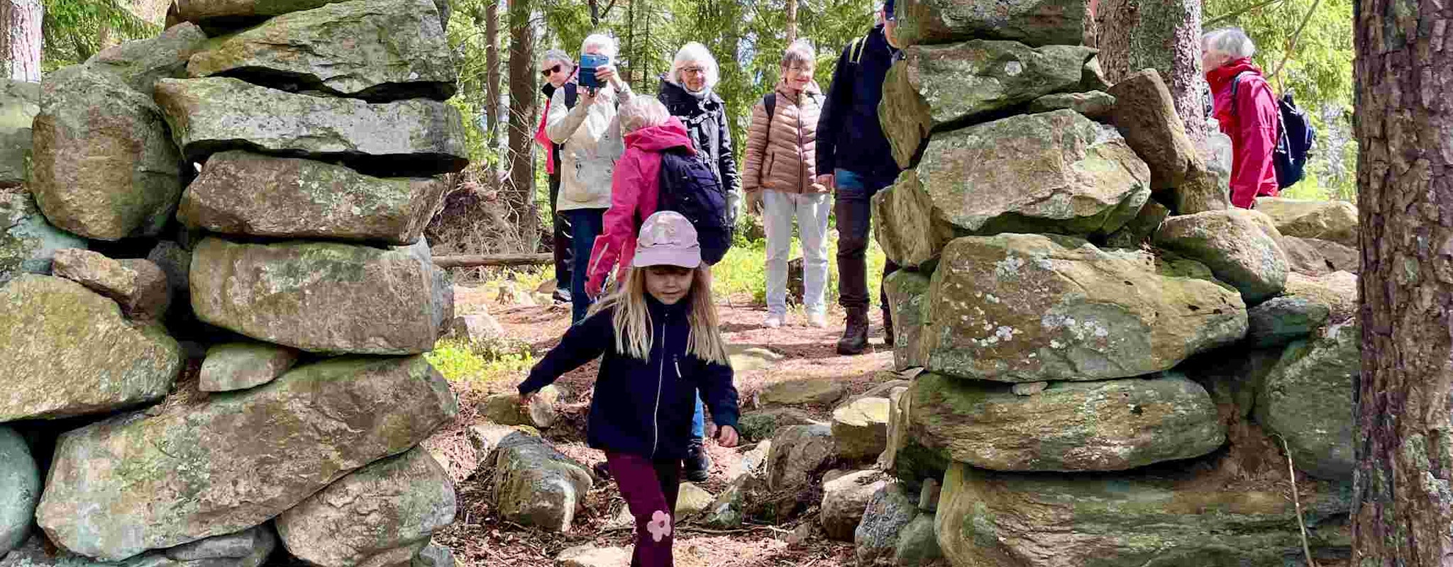 Barn leder en grupp vandrare genom en passage av stenar i skogen.