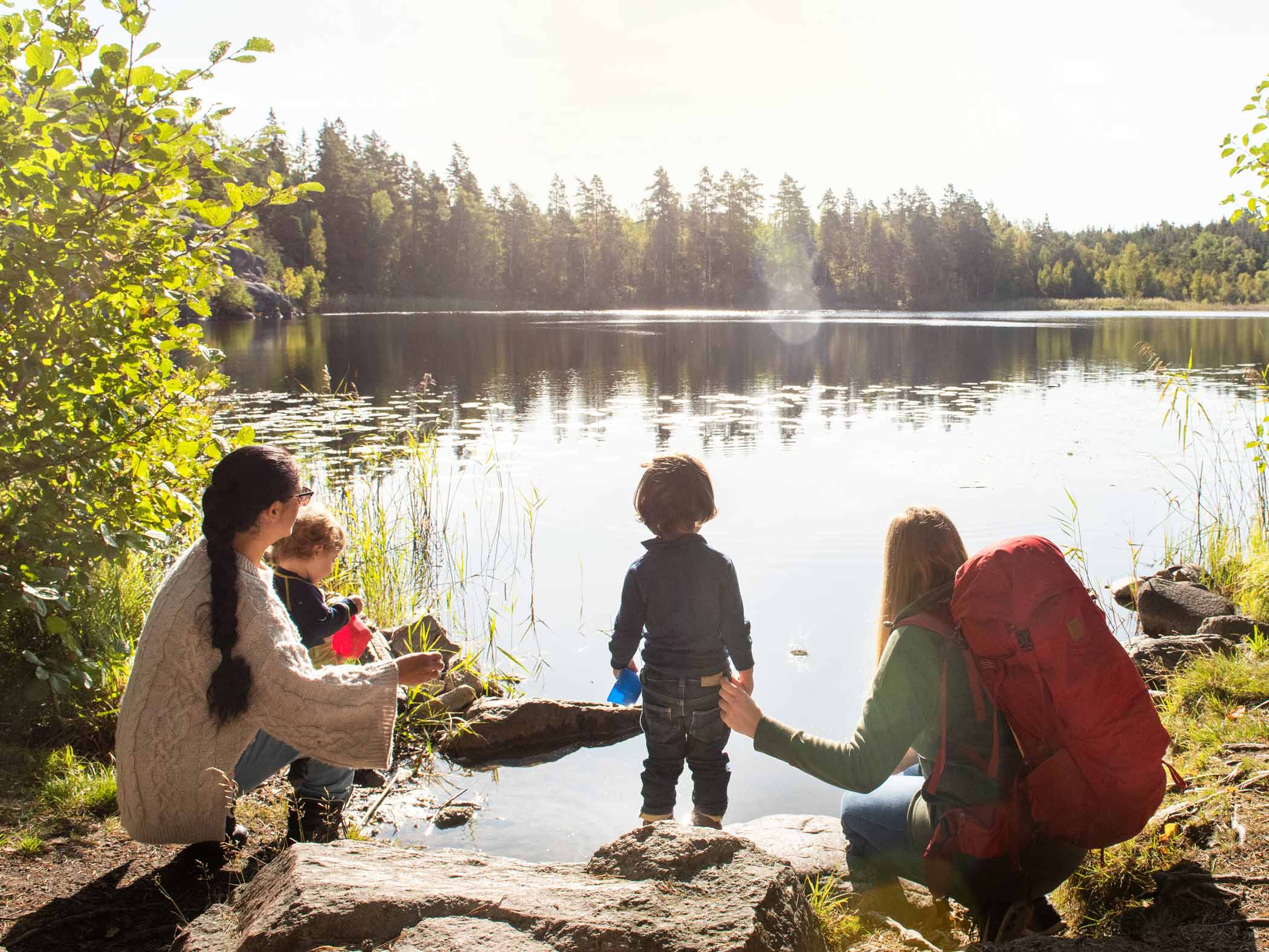Familj med barn sitter vid sjö i naturmiljö.