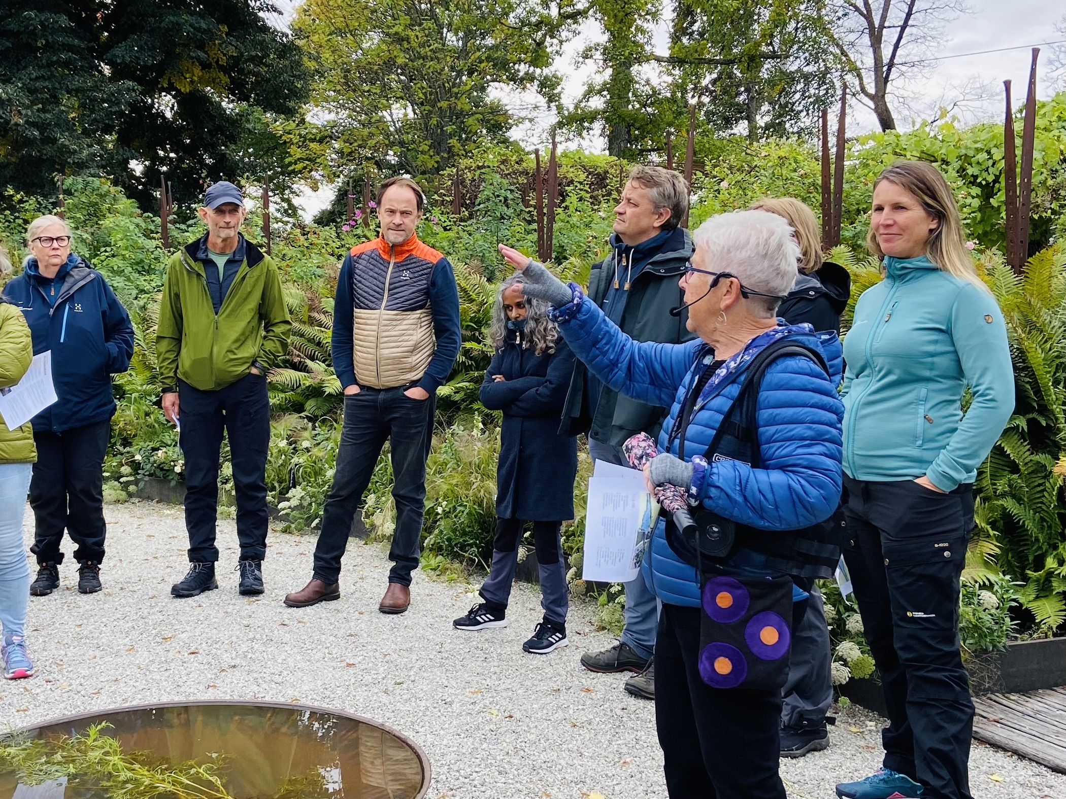 En guide pratat inför en grupp människor under en stadsvandring i en grönskande parkmiljö.