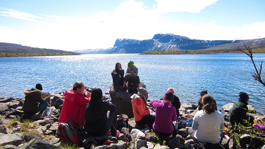 Ett tiotal tjejer har lunchpaus bredvid en fjällsjö