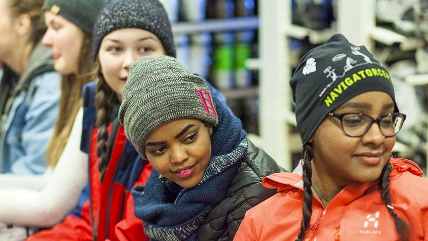 Fyra glada tonårstjejer i vinterkläder väntar tillsammans på en bänk