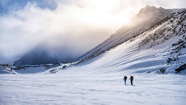 Skidåkare på avstånd intill snöklätt berg