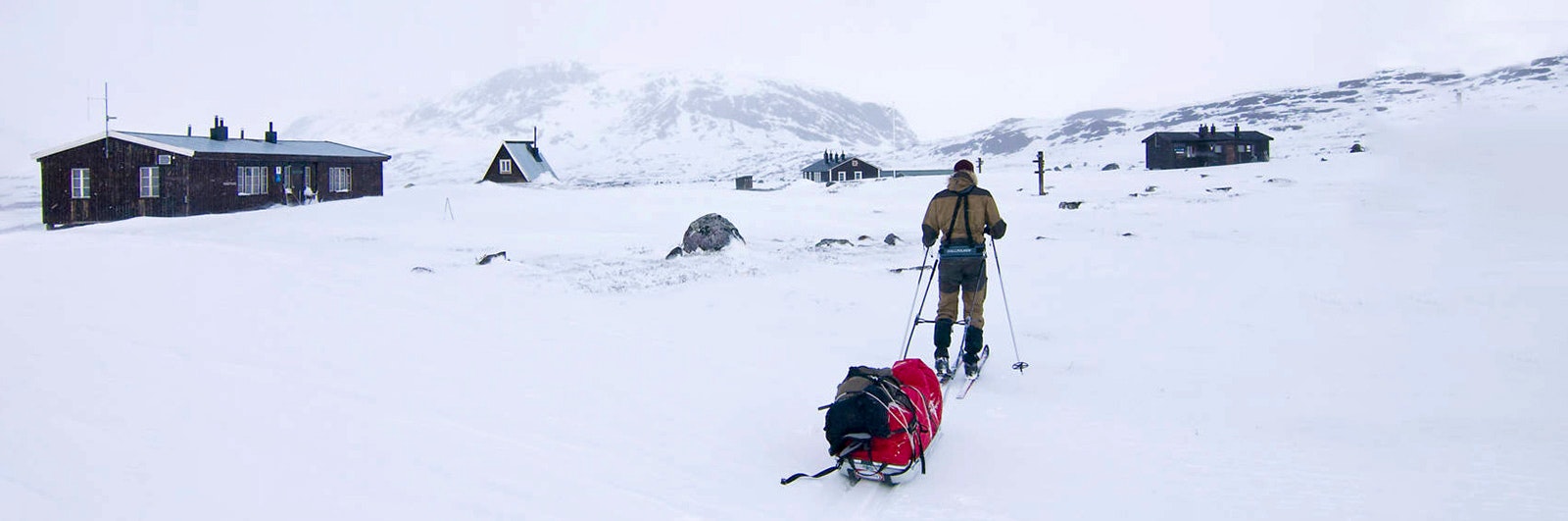 Skidåkare med pulka intill fjällstuga