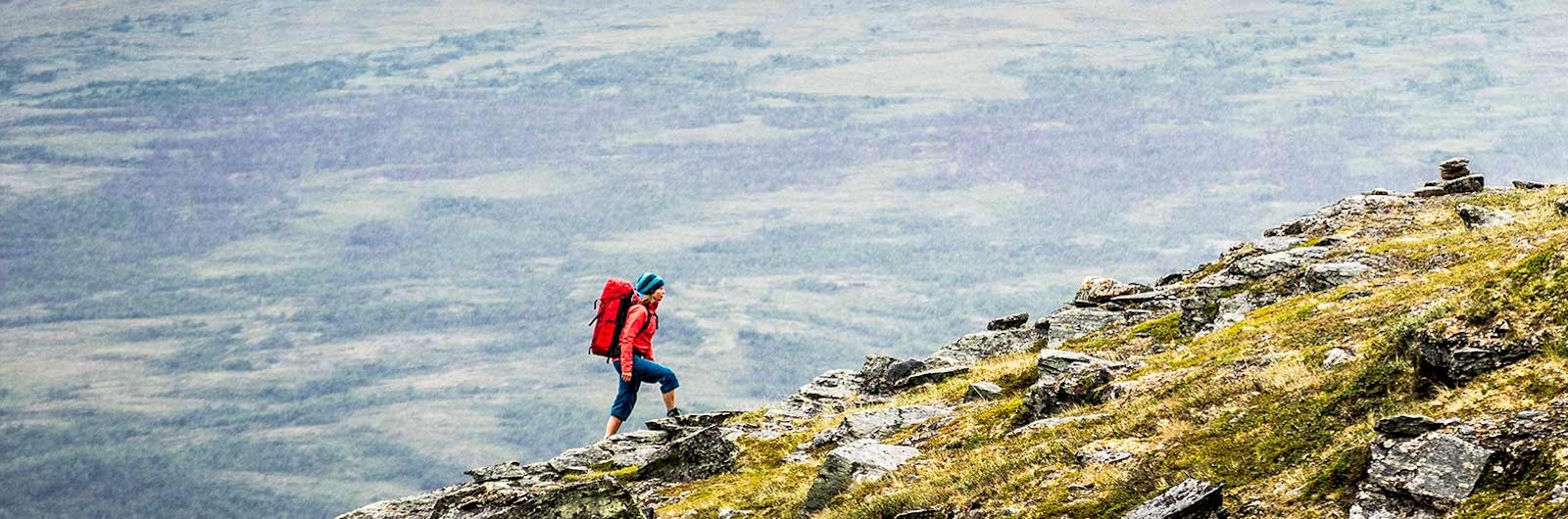 Kvinna vandrar på stupbrant berg längs Kungsleden