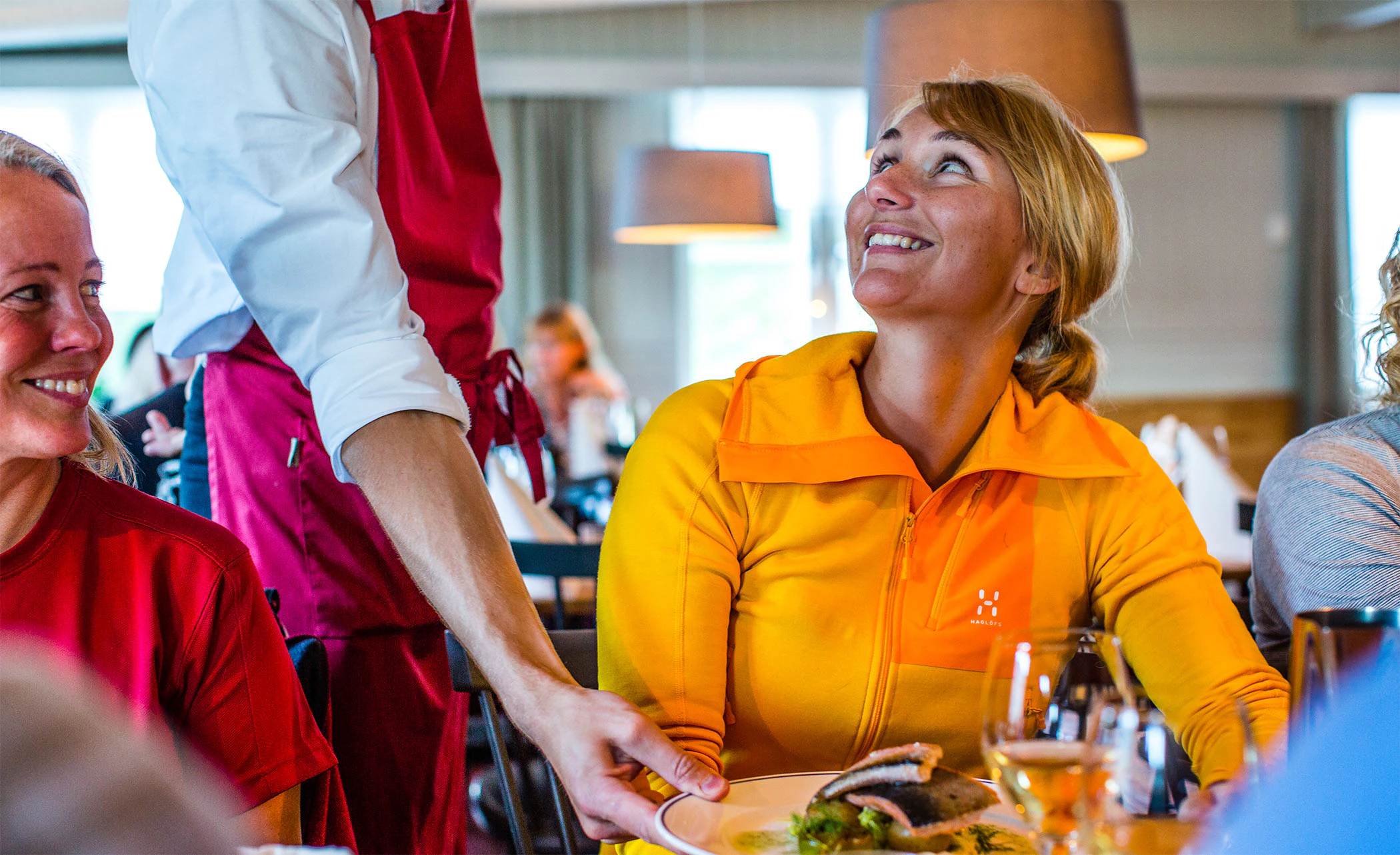 Gäster får mat serverad på en restaurang och samtalar glatt vid bordet.