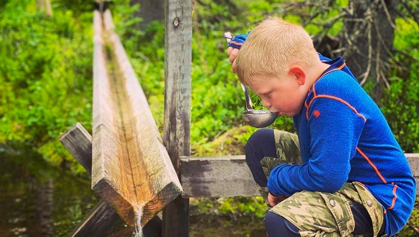 Pojke dricker vatten ur kåsa i skogen