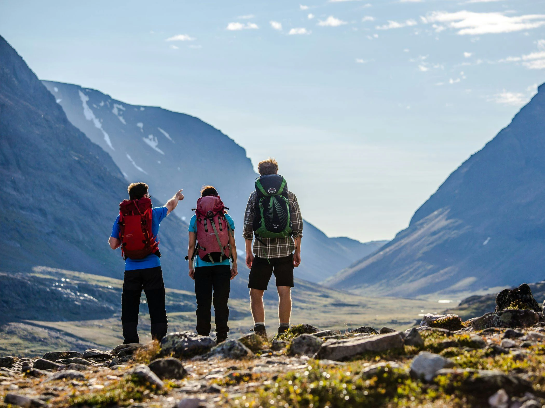 Vandrare på guidad tur blickar ut över dalgång mellan höga fjälltoppar i klart väder.