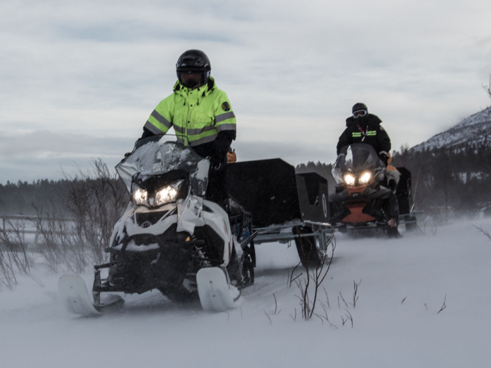 Två personer åker skoter till STF Saltoluokta Fjällstation i snötäckt landskap.