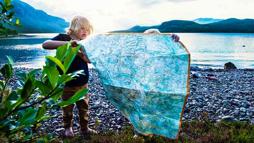 Två barn tittar på en stor karta vid sjön i Saltoluokta