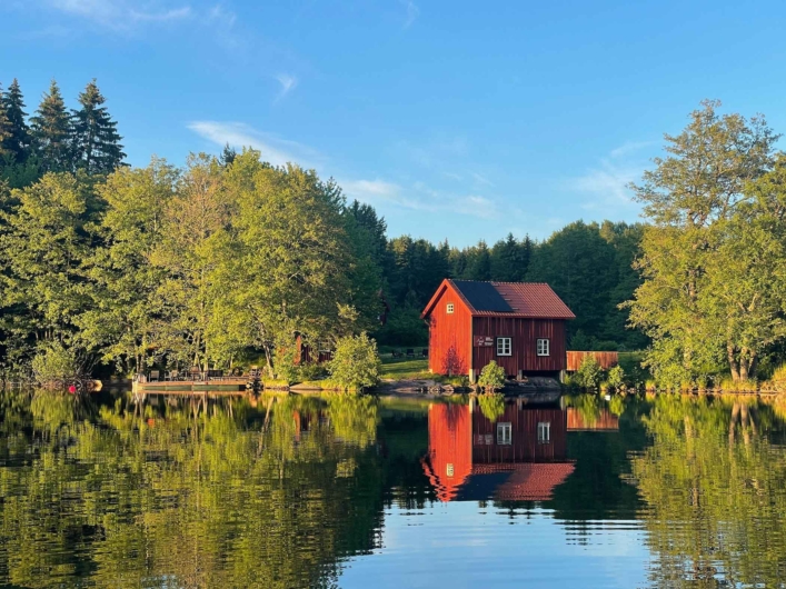 Röd stuga vid sjö.