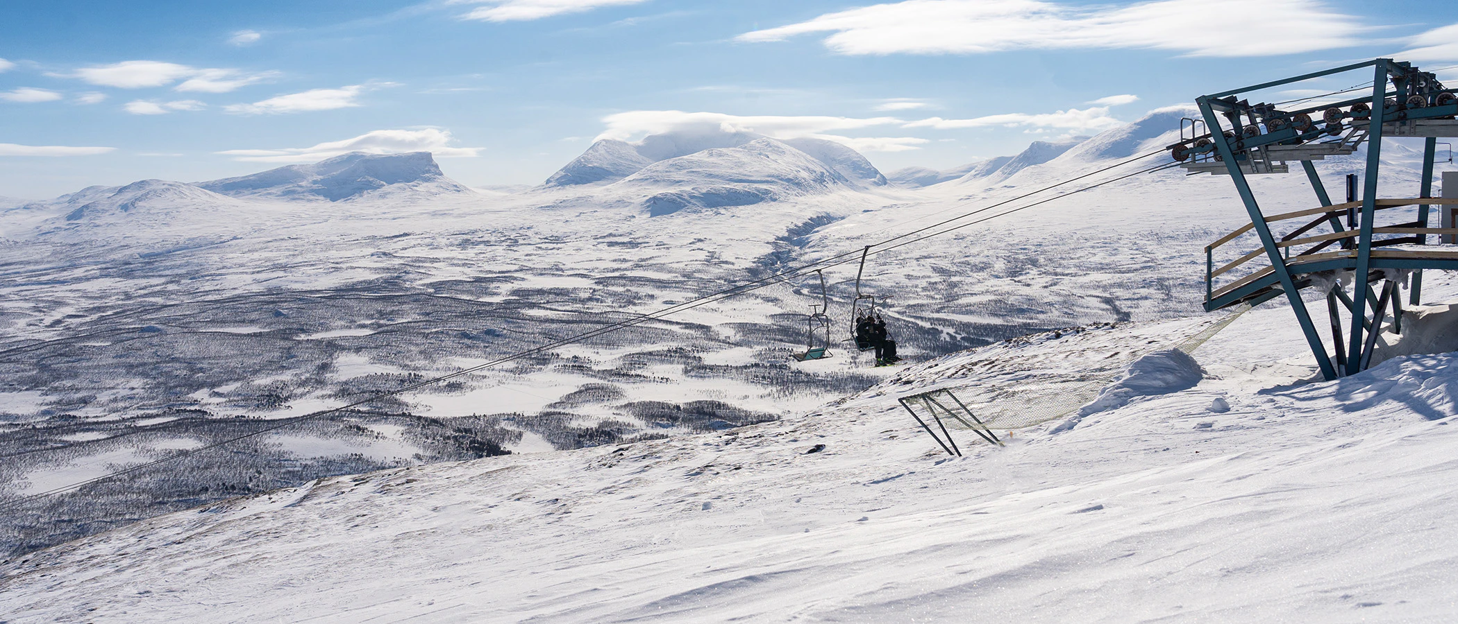 Snötäckt fjällandskap med skidlift och vy över dalen mot omgivande bergstoppar.