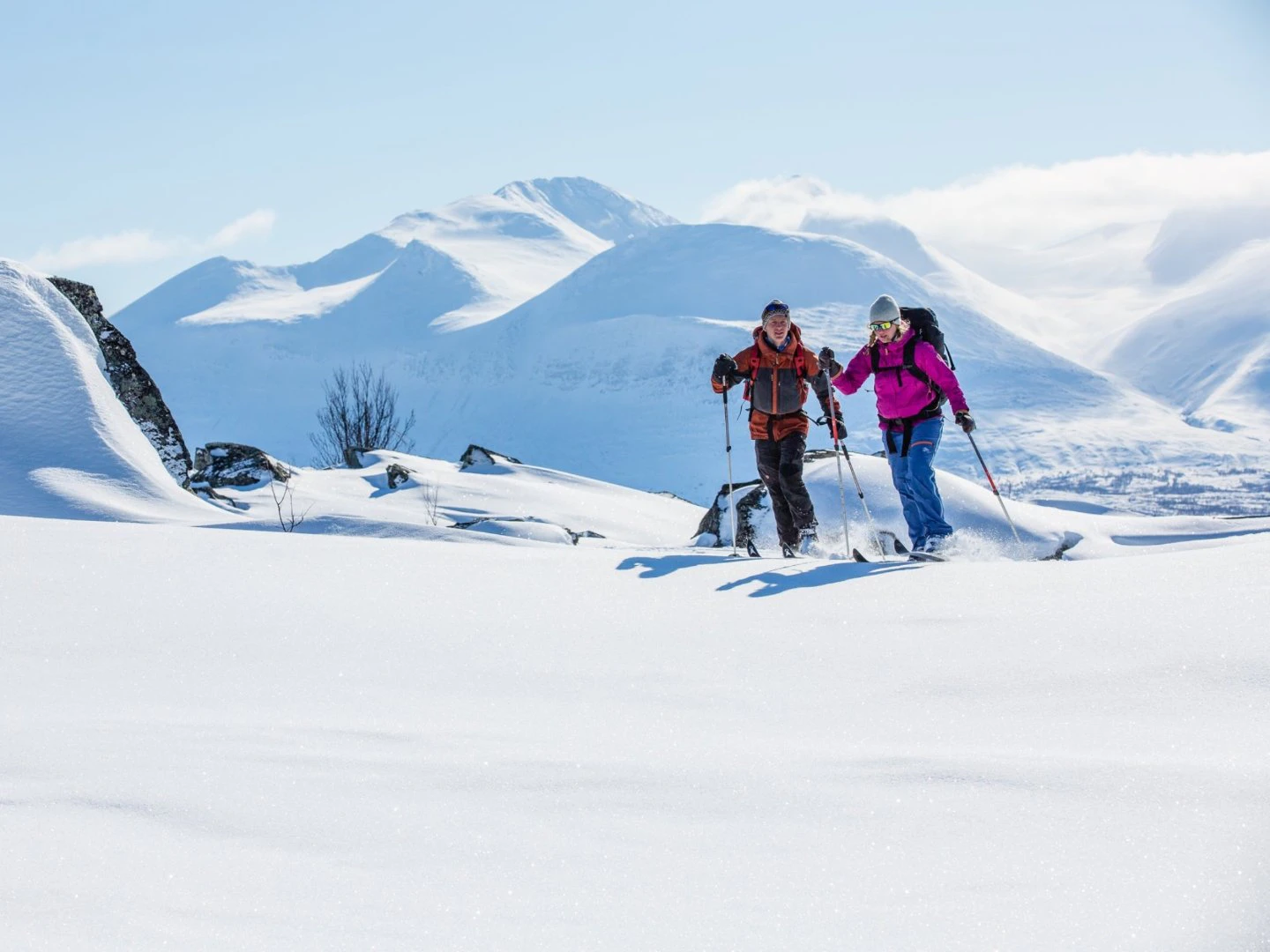 Två personer på fjälltur som turskidar över snötäckt landskap med berg i bakgrunden