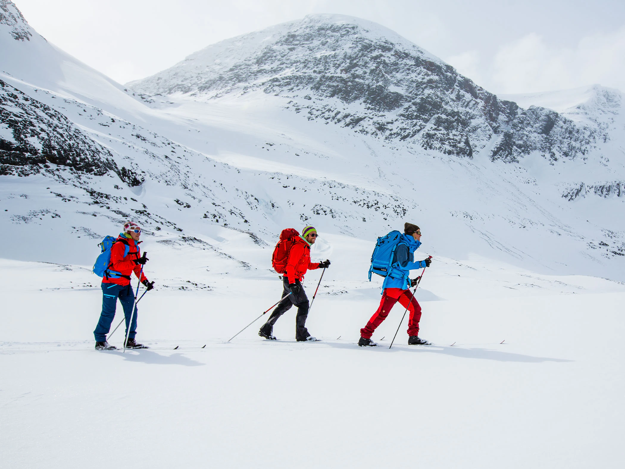 Tre skidåkare på fjälltur i snötäckt bergslandskap.