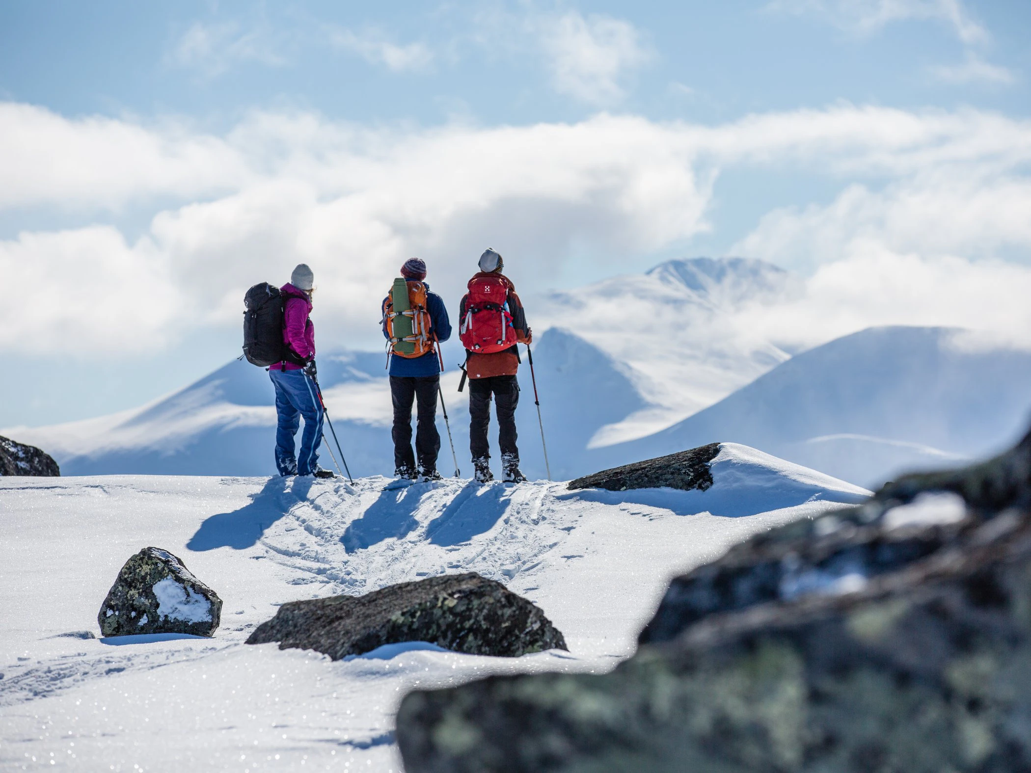 Tre skidåkare stannar på fjällkam och blickar ut över snötäckta berg.