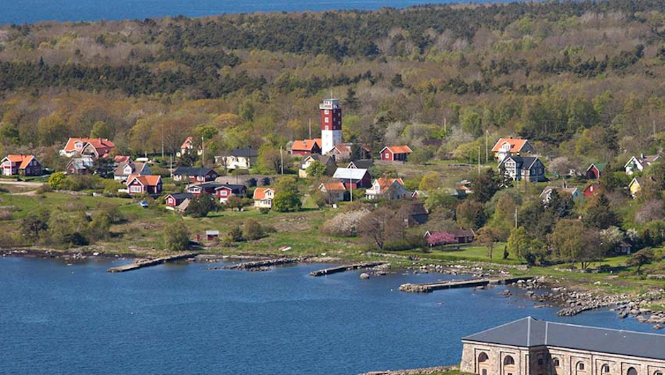 Vy över Lotstornet på Aspö omgivet av färgglada hus, grönskande landskap och kustlinje.