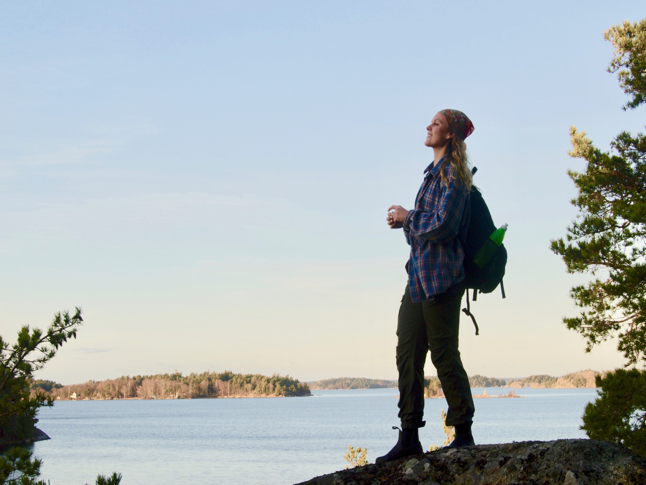 En person med ryggsäck står på klippa och blickar ut över hav och öar.