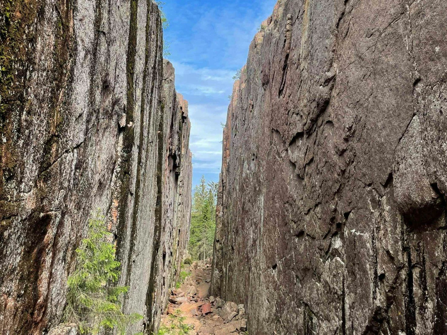 En dramatisk ravin med höga lodräta klippväggar leder fram mot en öppning där man kan skymta skog och himmel.
