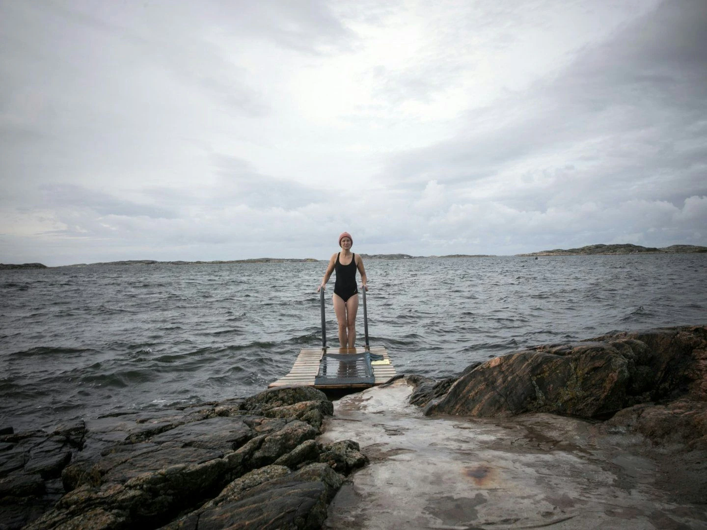 Kvinna i baddräkt står på brygga vid havet redo för kallbad.