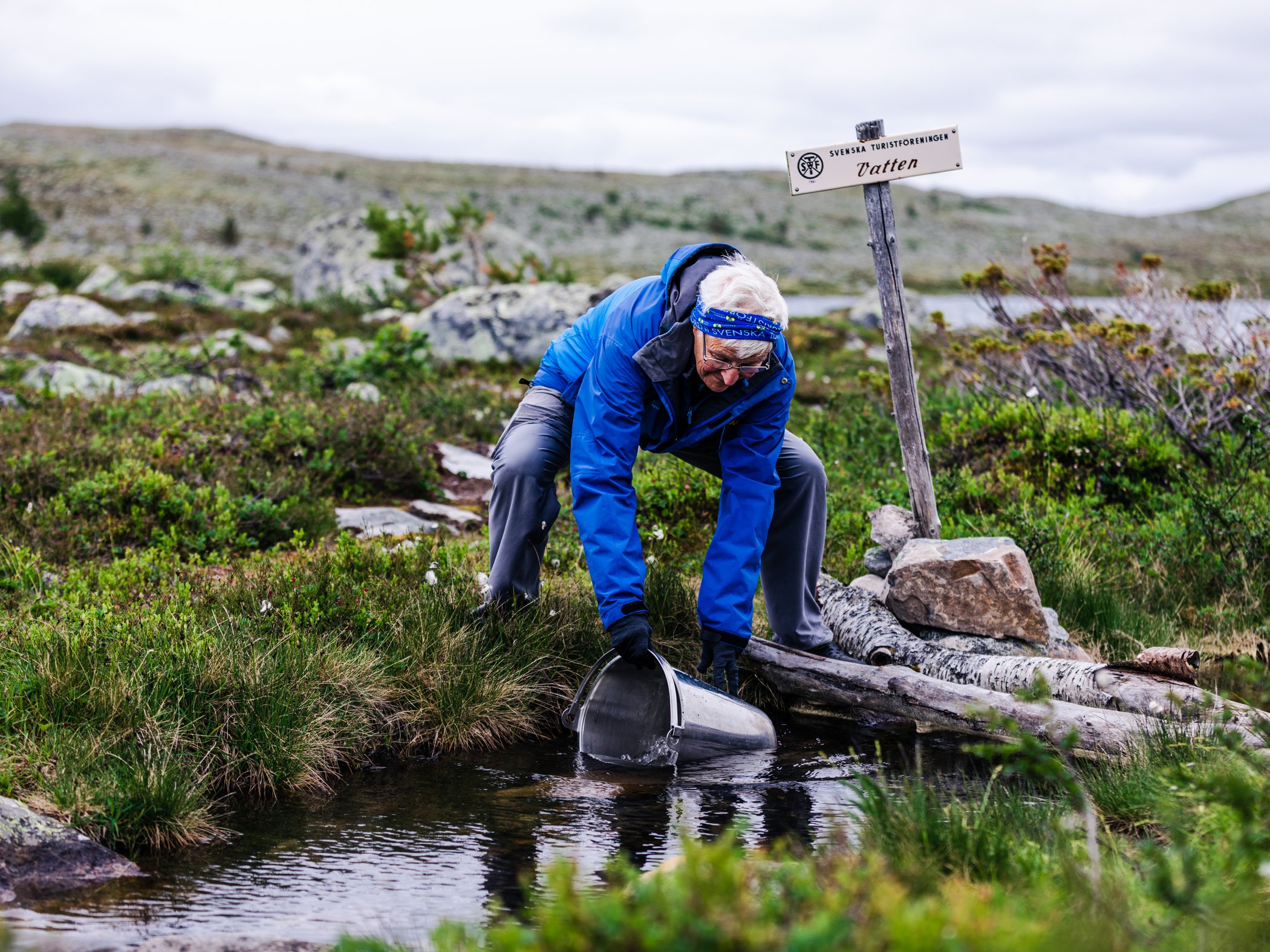 Kvinna hämtar vatten vid vattendrag i fjällen