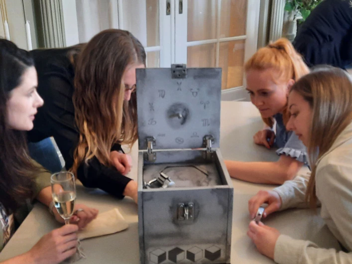 Fyra personer sitter runt en öppen låda med symboler på locket och undersöker innehållet tillsammans vid ett bord.