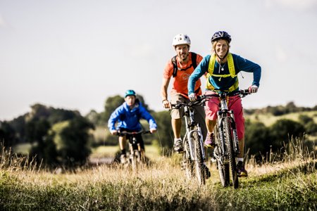 Tre personer cyklar mountain bike och tittar rakt in i kameran.
