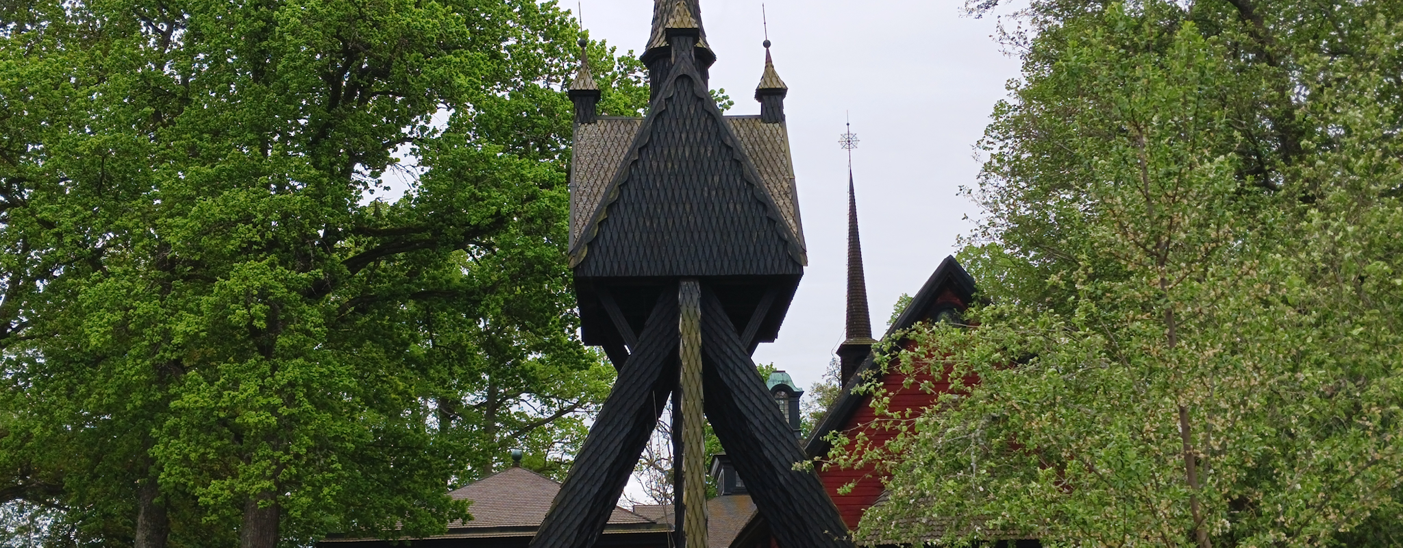 Rödsvart kyrka bland lummiga träd.