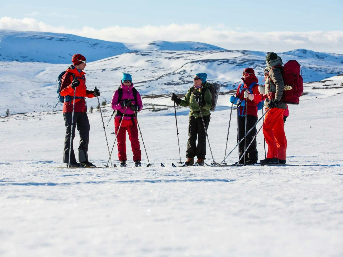Leende skidåkare i gul jacka med ryggsäck som vänder sig mot kameran under tur i snötäckt landskap