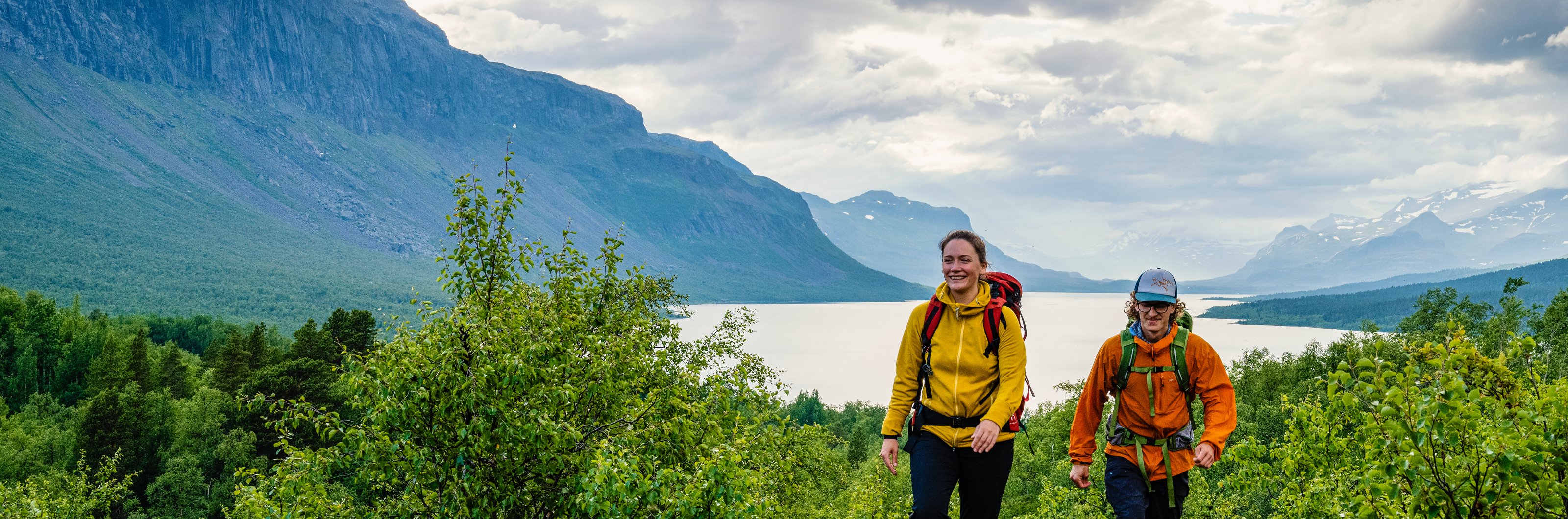 Två vandrare vandrar uppför en backe i Saltoluokta med fjällen i bakgrunden.