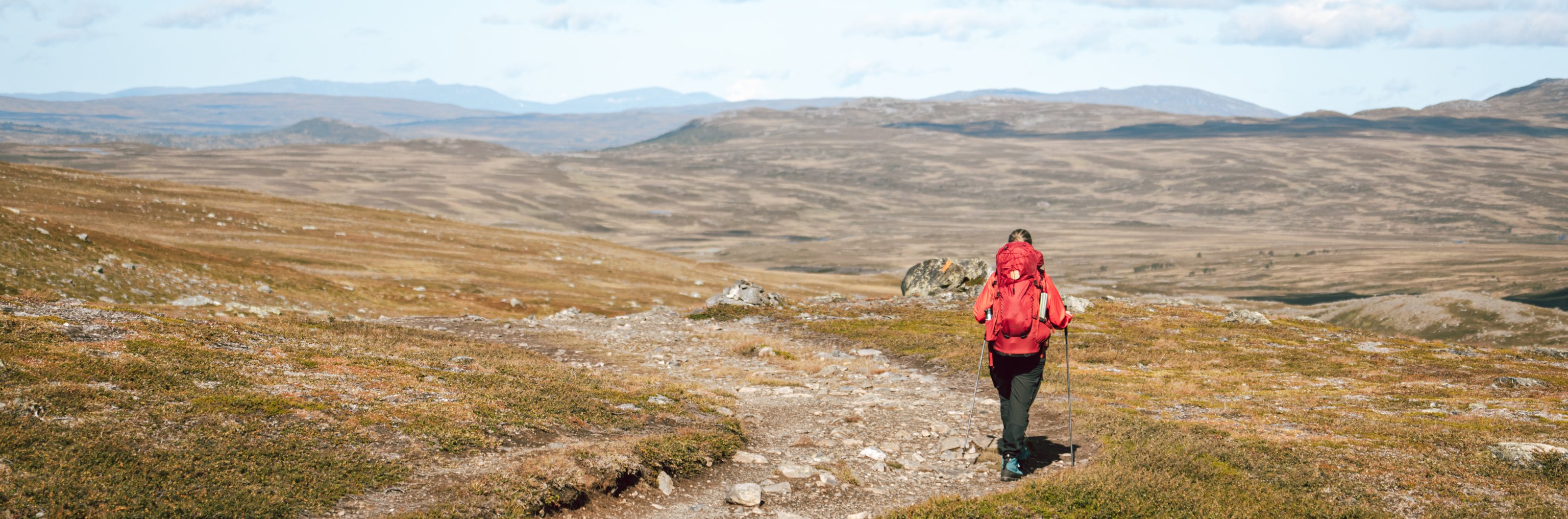 En kvinna vandrar på en stig i fjällen.