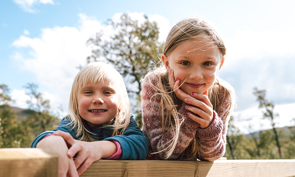 Två glada barn i friluftskläder ute i naturen.