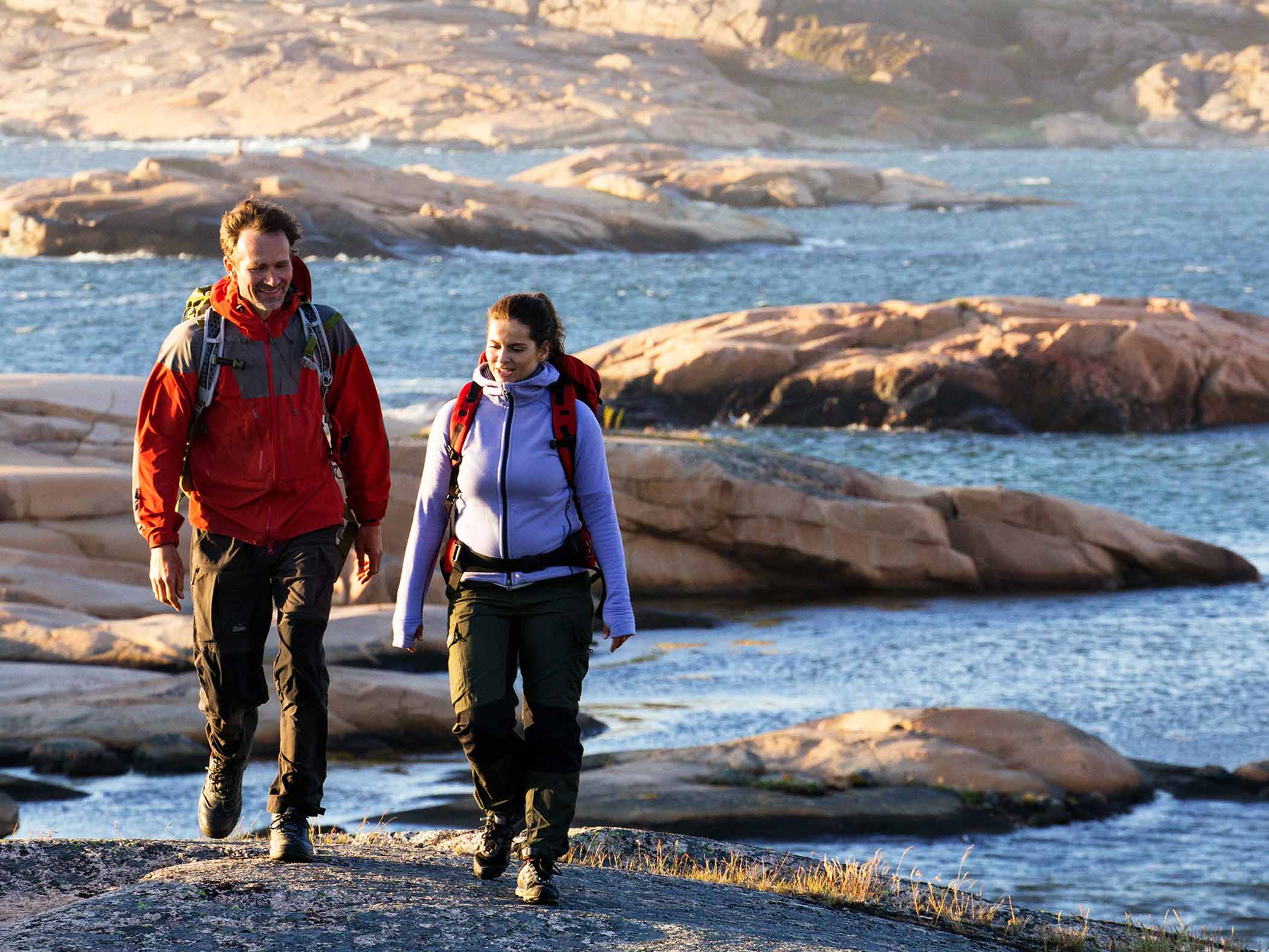 Två personer vandrar på klippor vid havet.