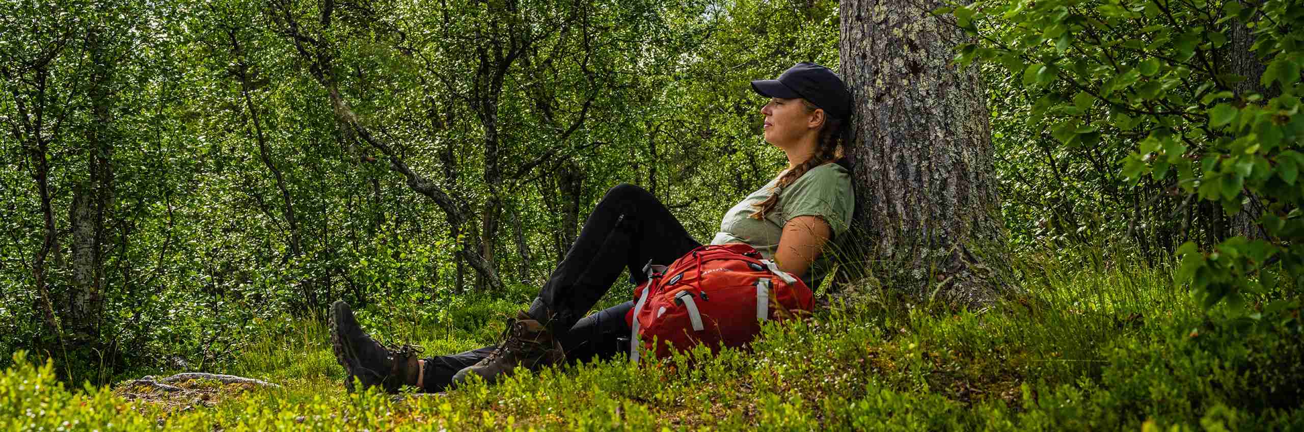 Kvinna kopplar av mot en trädstam i skogen.