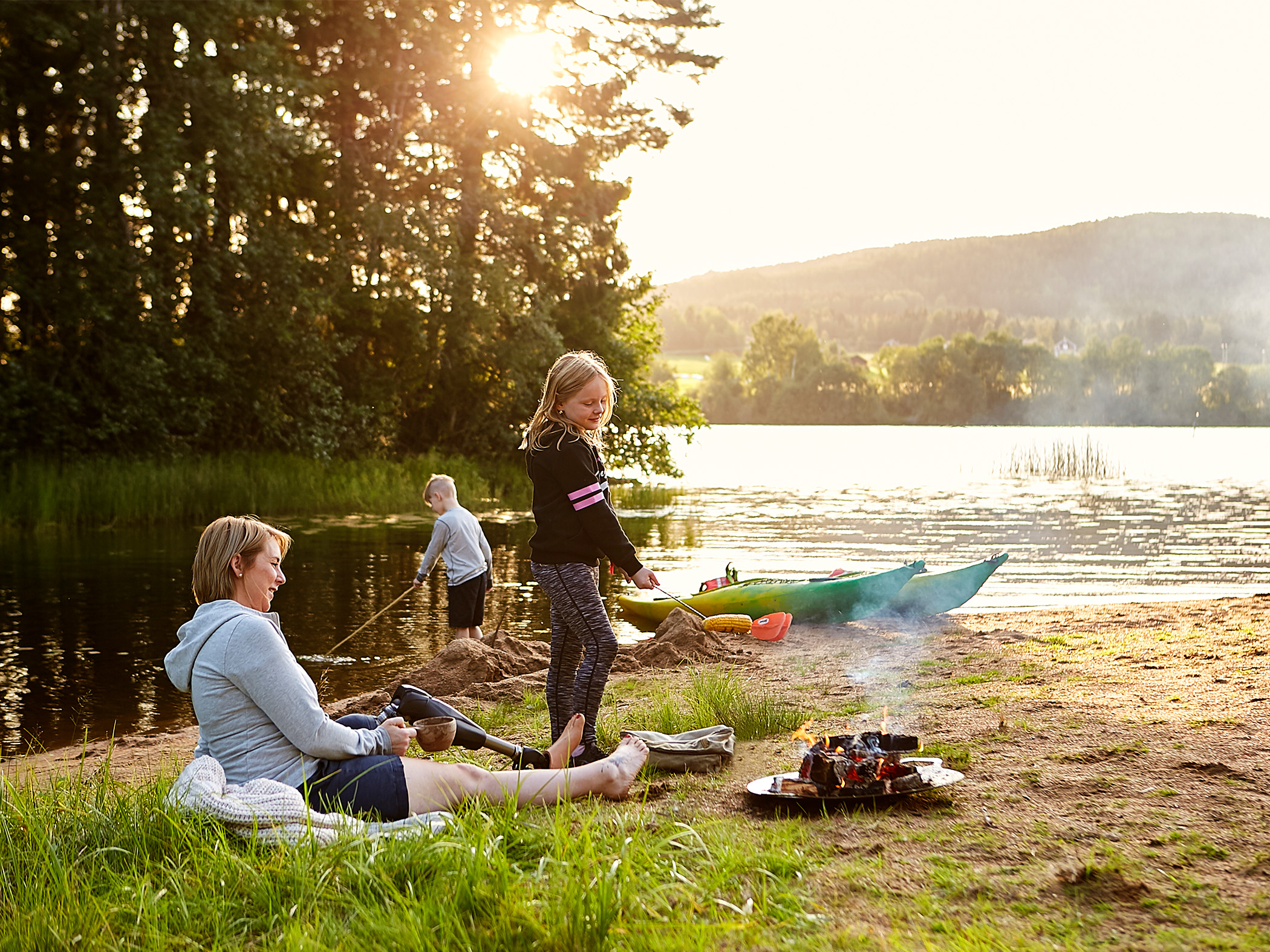 En barnfamilj grillar vid en strand med kanoter och älv i bakgrunden.
