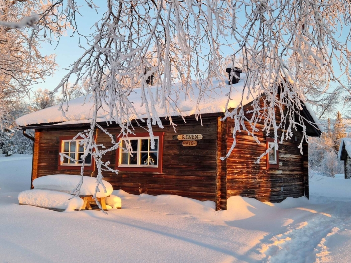 Stuga hos STF Fjällhornet med snö på taket och snöklätt träd framför. 