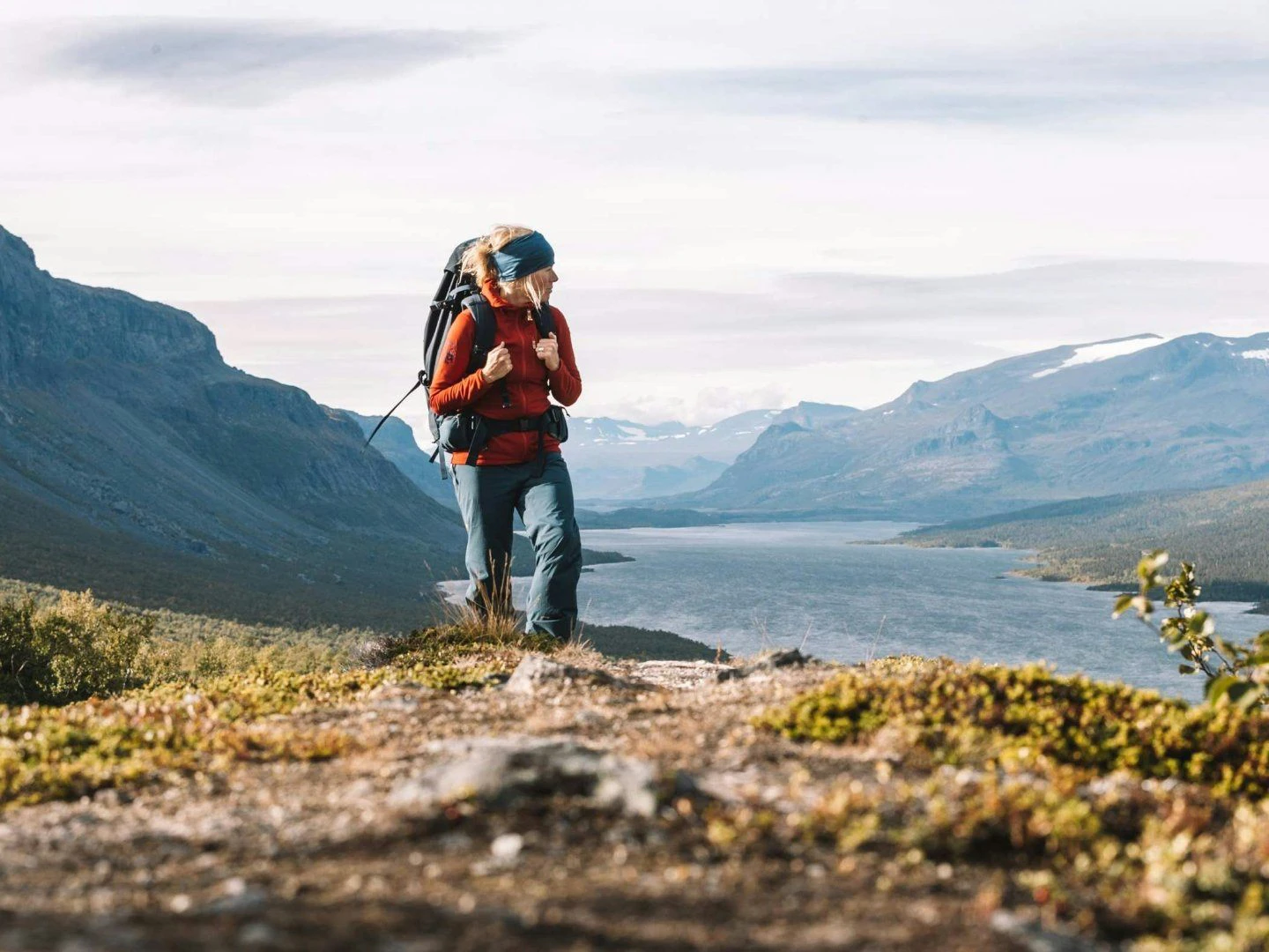 Person med ryggsäck vandrar på fjället med en sjö och berg i bakgrunden.