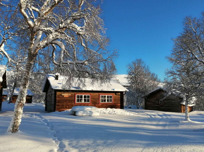 Stuga hos STF Fjällhornet med snö på taket och snöklätt träd framför.