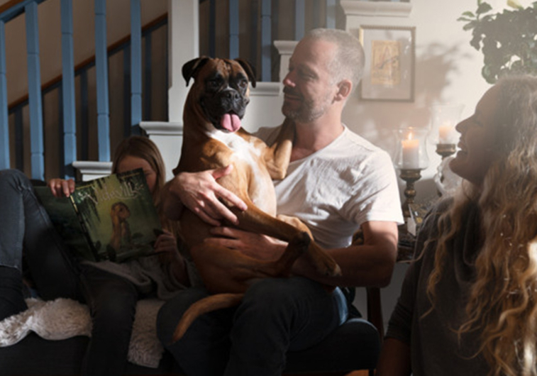 En boxerhund sitter i knät på sin husse omringad av resten av familjen.