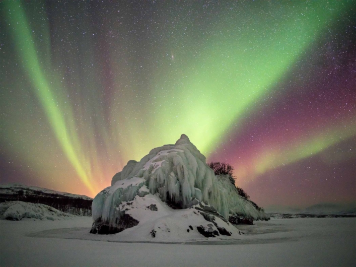 Norrsken som dansar över en klippformation i vinterlandskap. 