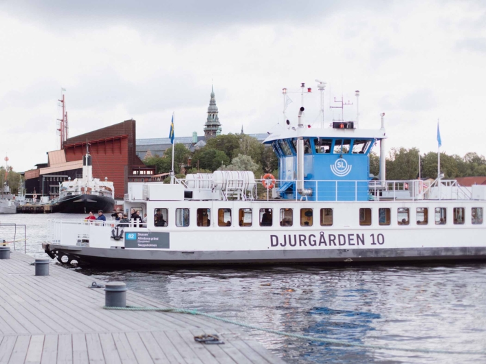 SL-färja ligger vid Skeppsholmen med passagerare ombord och Djurgårdens museer i bakgrunden.