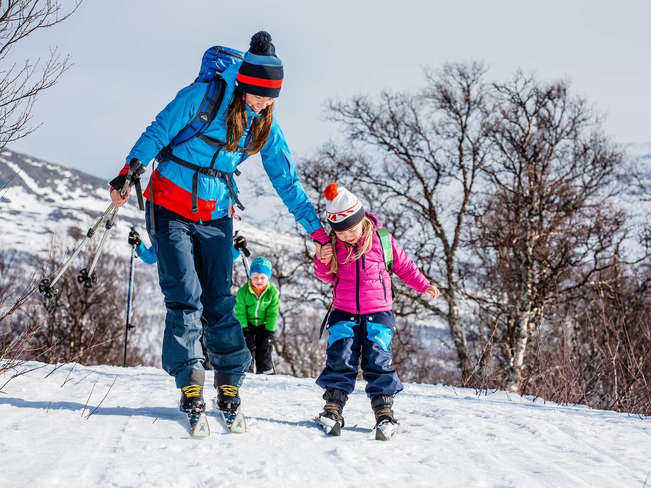 Vuxen och barn som åker turskidor tillsammans i soligt vinterlandskap vid Storulvån, med fler skidåkare bakom.
